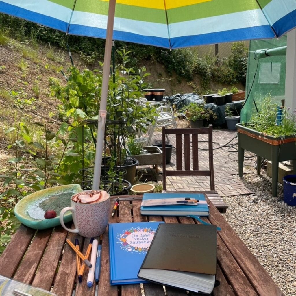 Gartentisch mit Sonnenschirm. Kaffetasse und Journals.