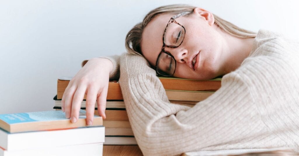 Eine erschöpfte Frau, die auf einem Stapel Büchern schläft